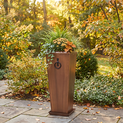 h potter brand tall rectangular planter with a decorative black metal pull handle, filled with green and yellow ornamental grasses, set on a stone patio in a sunlit garden.