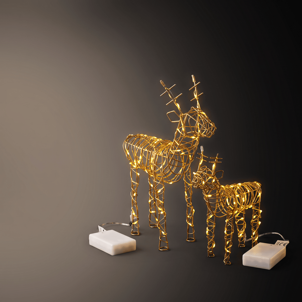 Two golden wire-frame deer sculptures with warm white LED lights, shown on a dark gradient background with two white battery packs.