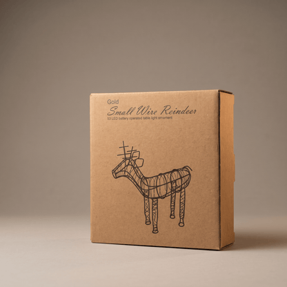 A square kraft paper box with a black line drawing of a reindeer and the text 'Gold Small Wire Reindeer' on the front, photographed against a plain warm gray studio background.