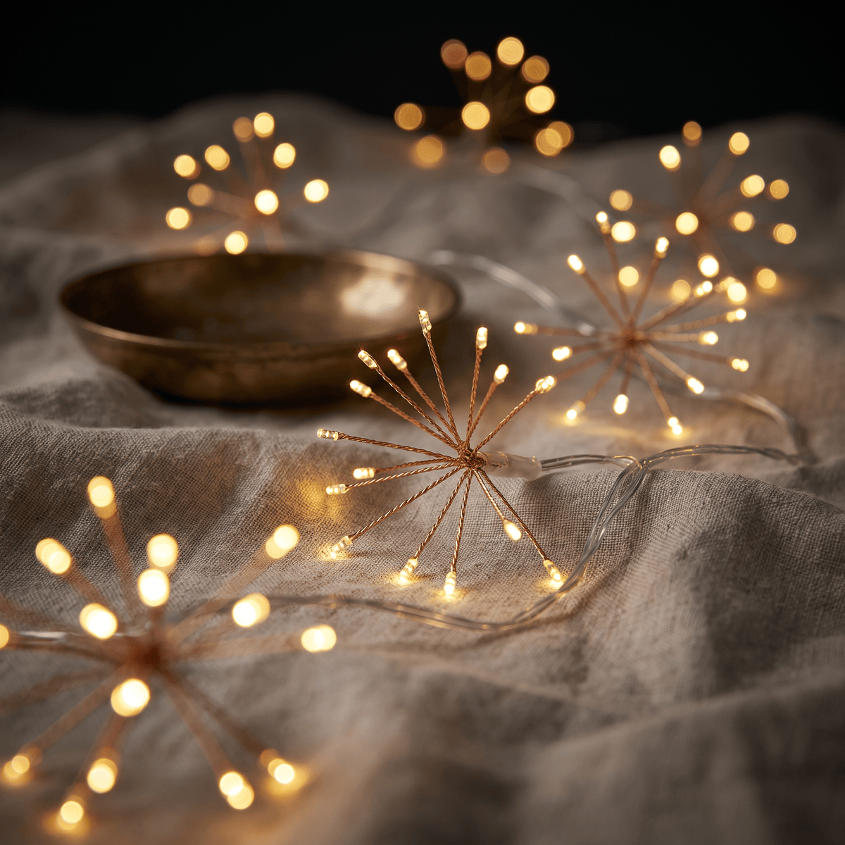 H POTTER sparkle  string fairy lights on copper wire glowing warmly on draped linen fabric, with a small brass bowl in the background.