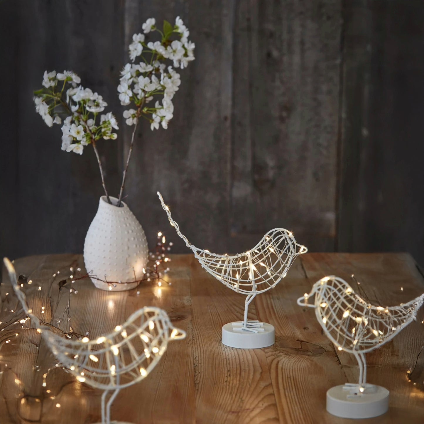 H Potter LED metal birds on a wooden surface, with a vase of white flowers in the background.