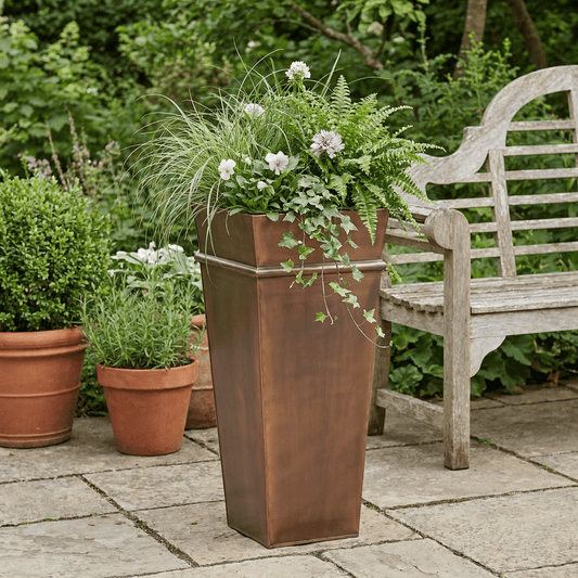 h potter tall antique copper planter on stone patio with flowers and ferns