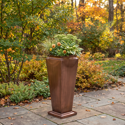 h potter brand tall planter with a tiered base, filled with green foliage and small orange flowers, set on a stone patio in an autumn garden.