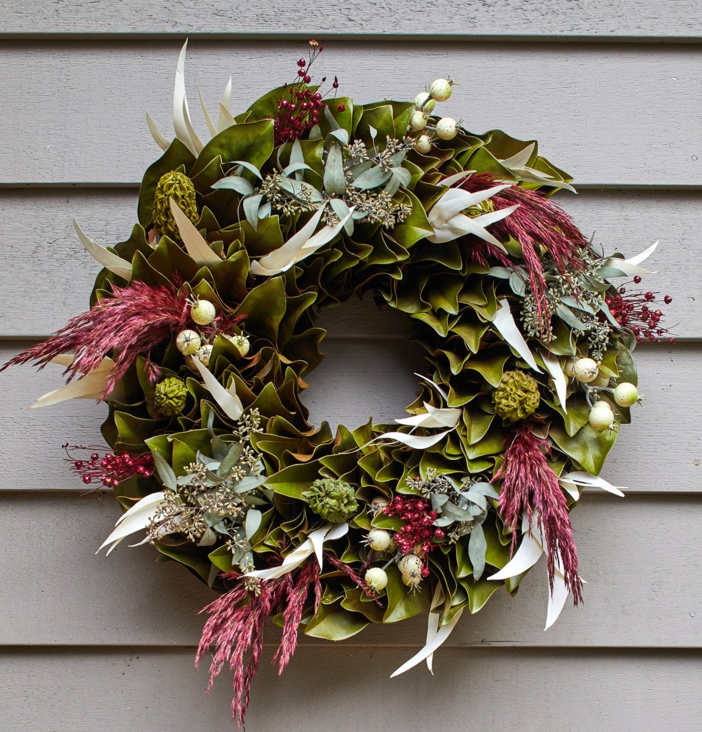 h potter woodland magnolia decorative wreath with green leaves, red berries, and white feathers on a neutral background