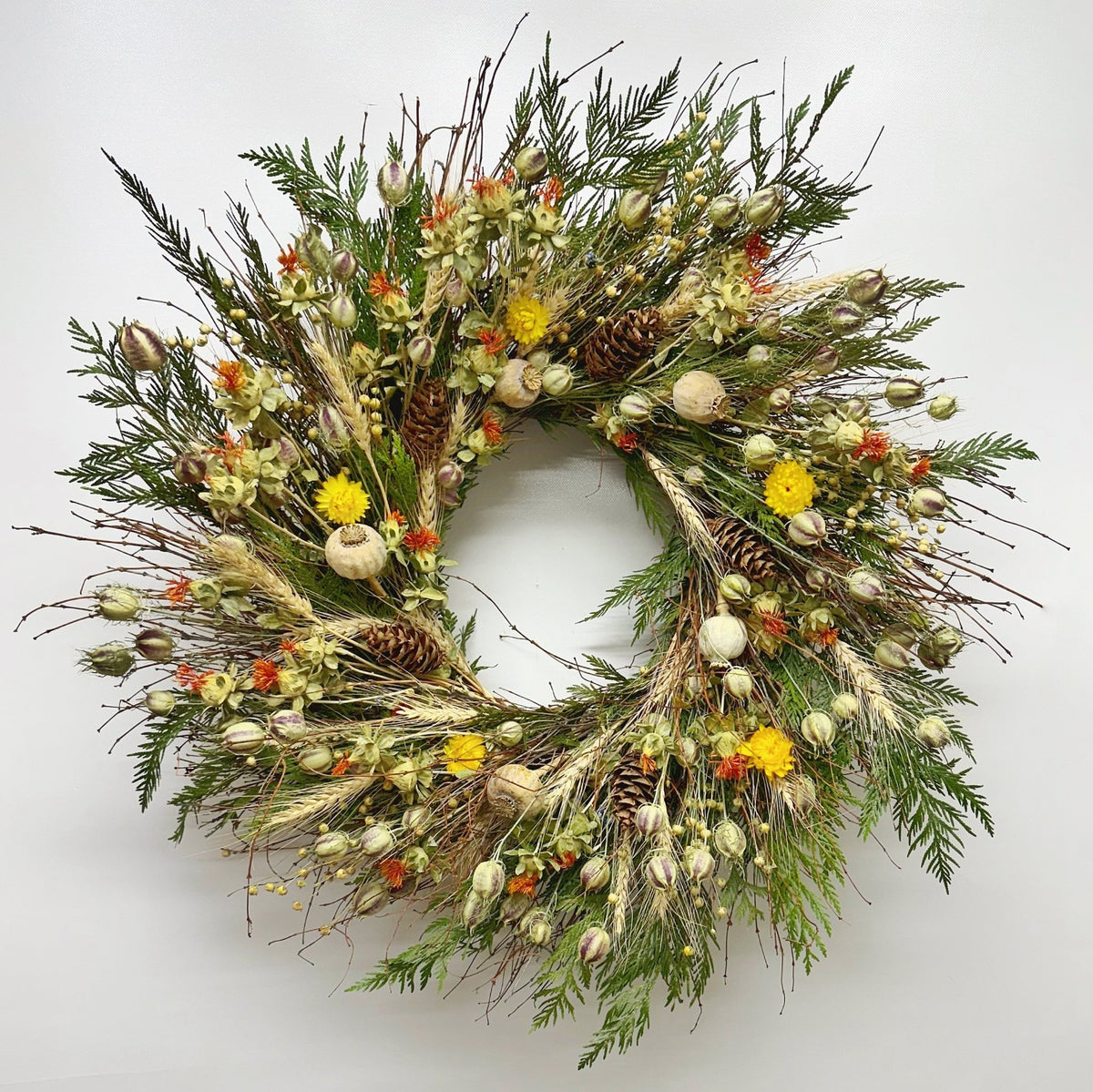 Autumn bramble wreath on wall—handmade H Potter dried botanicals: twigs, cedar, wheat, safflower, strawflower, pine cones.