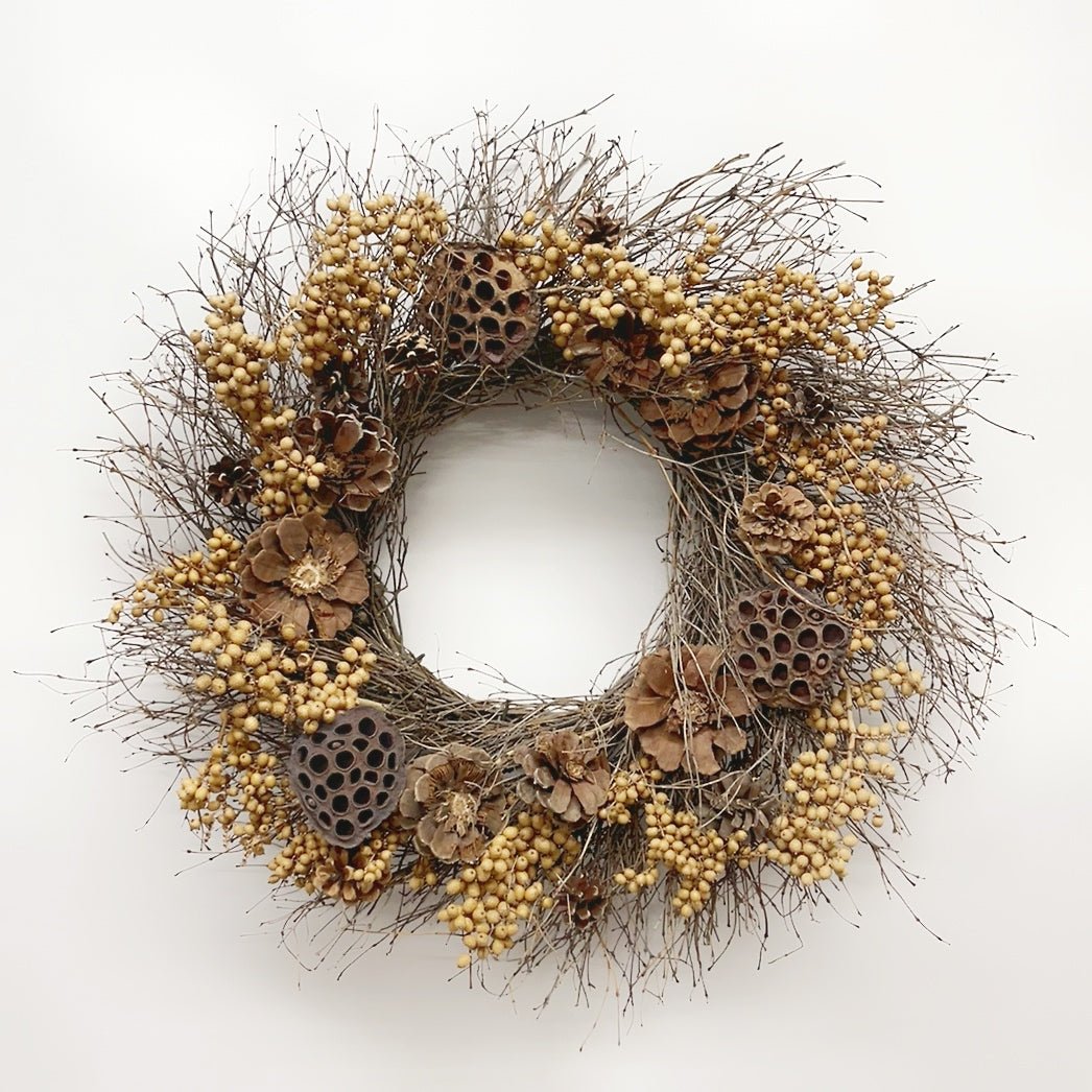 A rustic dried botanical wreath featuring natural twig branches, small beige berries, brown pinecones, and dried lotus pods, displayed against a clean white background.