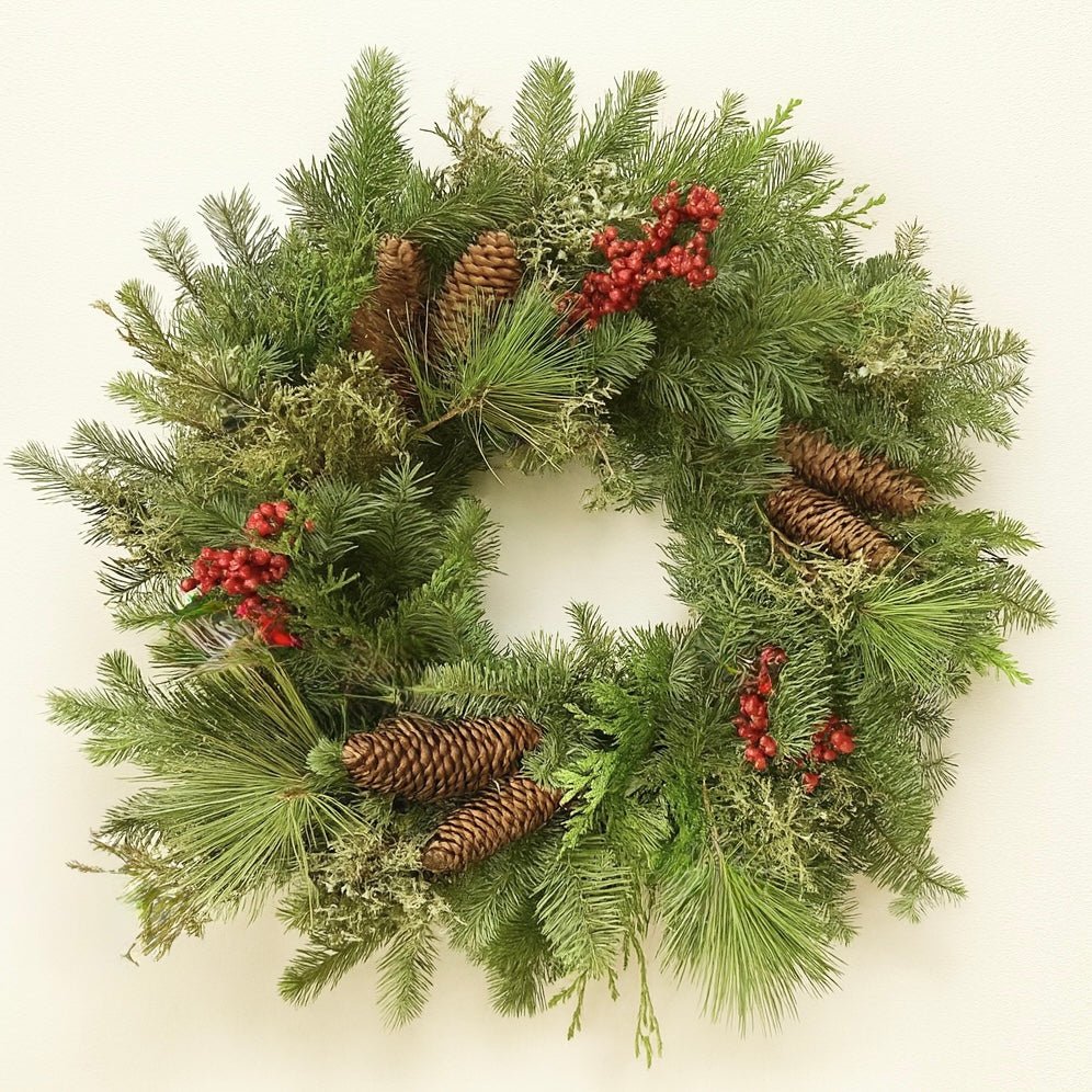 Christmas wreath with greenery, pinecones, and red berries on a white background