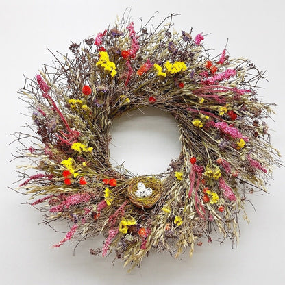 spring wreath with yellow and pink flowers and a birds nest on a white background