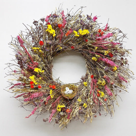 spring wreath with yellow and pink flowers and a birds nest on a white background