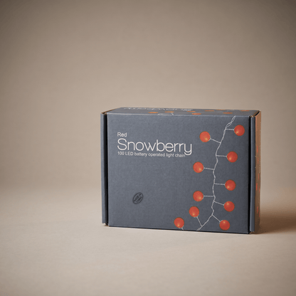 A dark gray cardboard box for 'Red Snowberry' 100 LED battery operated light strings, featuring illustrations of red berries on a white branch, set against a solid beige background.